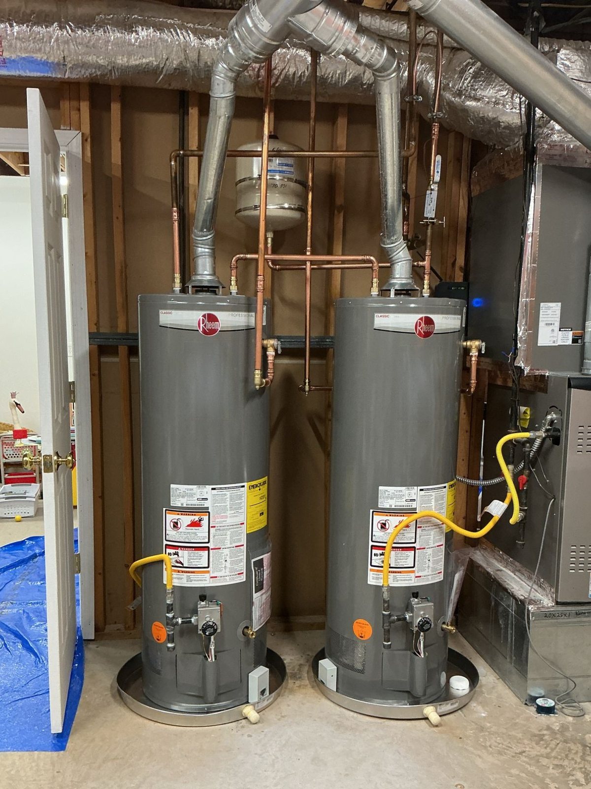 Two gas tank water heaters installed side by side in drain pans, with new copper and gas lines