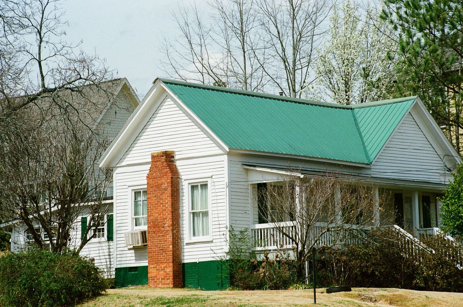 White cottage with a green metal roof and a brick chimney
